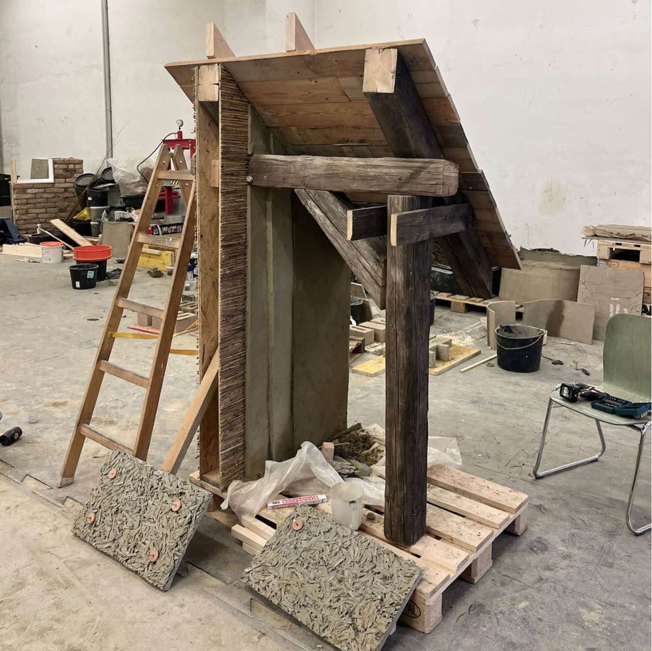 The mock-up under construction, test panels leaning against pallets in front of the timber frame